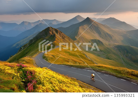 Cyclist with Backpack Riding Through Scenic Landscape in Majestic Mountain Range at Sunrise Cyclist with Backpack Riding Through Scenic Landscape in Majestic Mountain Range at Sunrise 135993321