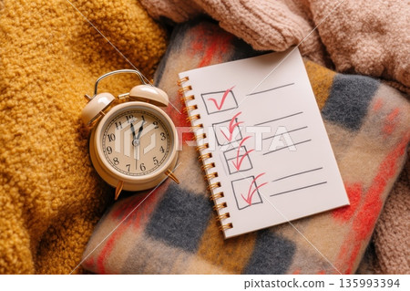 Classic Alarm Clock Beside a Checklist on a Cozy Blanket in a Warm Atmosphere 135993394