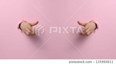 Two female hands reach out to each other through torn holes in bright pink paper against a backdrop of empty space. Two female hands reach out to each other through torn holes in bright pink paper against a backdrop of empty space. 135993611