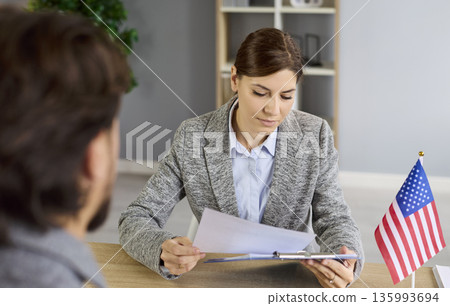 Consular visa interview, discussion of lawyer and man at office desk with US flag 135993694