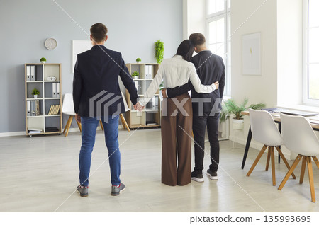 Office love triangle as woman hugs one colleague and secretly holds another's hand 135993695