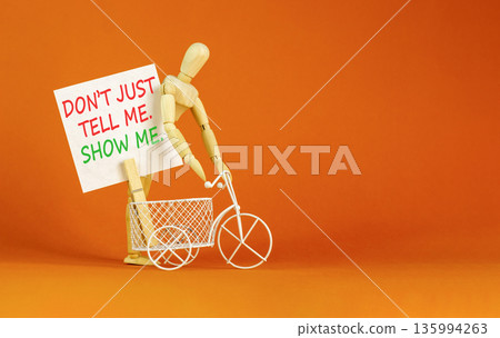 Tell or show symbol. Concept words Do not just tell me, show me on beautiful white paper. Beautiful orange background. Miniature bicycle. Businessman's model. Business tell or show concept. Copy space Tell or show symbol. Concept words Do not just tell me, show me on beautiful white paper. Beautiful orange background. Miniature bicycle. Businessman's model. Business tell or show concept. Copy space 135994263
