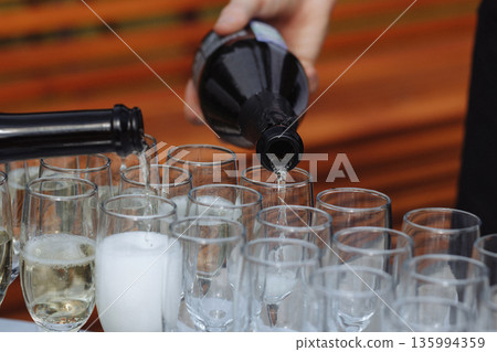 Adult hand pouring champagne into glasses on event table with wooden background Adult hand pouring champagne into glasses on event table with wooden background 135994359