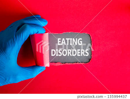 Eating disorders symbol. Concept words Eating disorders on beautiful grey paper. Doctor hand in blue medical glove. Beautiful red background. Medical healthy lifestyle eating disorders concept. Eating disorders symbol. Concept words Eating disorders on beautiful grey paper. Doctor hand in blue medical glove. Beautiful red background. Medical healthy lifestyle eating disorders concept. 135994437
