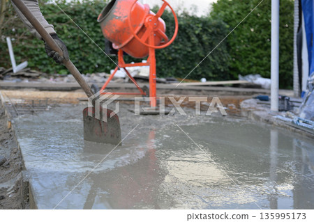 Worker Pouring and Spreading Fresh Concrete Slab in Formwor. 135995173