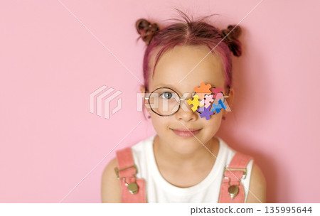 Portrait of a young girl wearing glasses with colorful puzzle pieces covering one eye. Visual concept of autism awareness, inclusion, neurodiversity, empathy and child development in studio setting. 135995644