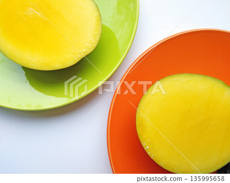 Two halves of a ripe, juicy mango lie on plates against a white background 135995658