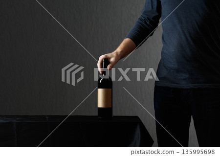 Man picks up a bottle of red wine with empty label. Man picks up a bottle of red wine with empty label. 135995698