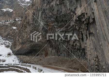 Towering vertical basalt columns form monumental cliff at Symphony of Stones, dramatic volcanic geometry rises above a winter road 135995711
