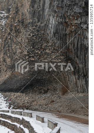 Snow-covered road curves along massive basalt cliffs at Symphony of Stones, layered volcanic rock and stone barriers shape dramatic winter landscape. Snow-covered road curves along massive basalt cliffs at Symphony of Stones, layered volcanic rock and stone barriers shape dramatic winter landscape. 135995714