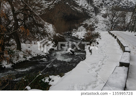 Winter river flows through snow-covered banks beneath rocky cliffs at the Symphony of Stones, dark moving water contrasts with white snow Winter river flows through snow-covered banks beneath rocky cliffs at the Symphony of Stones, dark moving water contrasts with white snow 135995728