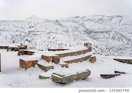 Snow-covered stone ruins stand near the Garni Temple, broken walls and ancient blocks contrast with the wide winter mountain landscape Snow-covered stone ruins stand near the Garni Temple, broken walls and ancient blocks contrast with the wide winter mountain landscape 135995749