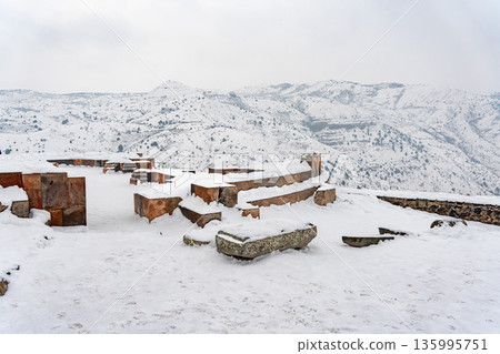 Snow-covered stone ruins stand near the Garni Temple, broken walls and ancient blocks contrast with the wide winter mountain landscape Snow-covered stone ruins stand near the Garni Temple, broken walls and ancient blocks contrast with the wide winter mountain landscape 135995751