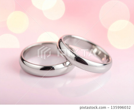 一對閃亮的鉑金戒指,背景是粉紅色的。 一對閃亮的鉑金戒指,背景是粉紅色的。 135996032