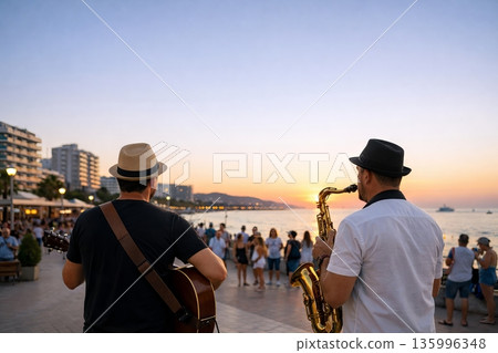 Two men, a guitarist and a saxophonist, performing street music for an audience at sunset. Live entertainment and busking concept 135996348