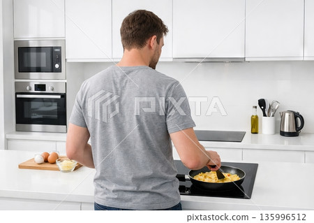 Man cooking in a modern kitchen, stirring food in a frying pan on an induction hob. Healthy eating and home cooking concept 135996512