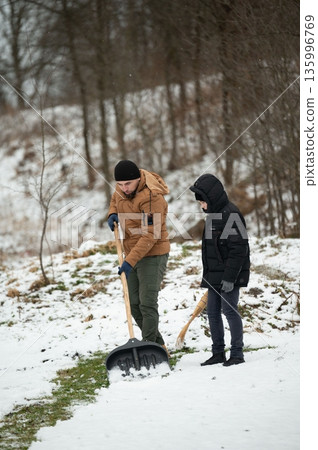 Father and son teamwork shoveling snow in a wintery landscape. A shared chore, strengthening bonds. Father and son teamwork shoveling snow in a wintery landscape. A shared chore, strengthening bonds. 135996769