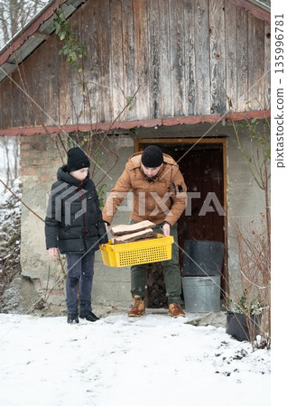 Father and son carry firewood in the snow. Father and son carry firewood in the snow. 135996781
