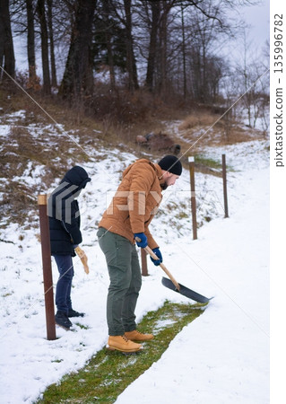 Two individuals collaborate on snow removal, diligently clearing a pathway in a snowy landscape. 135996782
