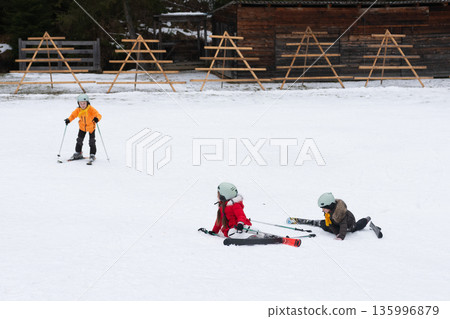 Joyful moments of children learning to ski in a snowy landscape surrounded by wooden ski racks on a crisp winter day Joyful moments of children learning to ski in a snowy landscape surrounded by wooden ski racks on a crisp winter day 135996879