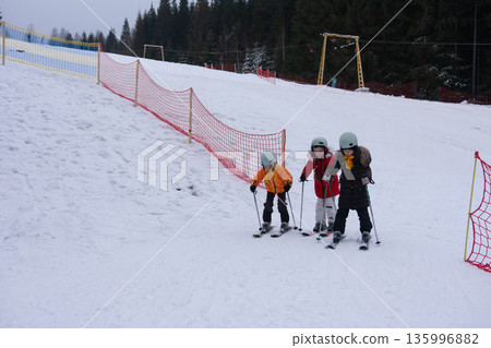 Excitement fills the air as children learn to ski on a snowy slope surrounded by trees in a winter wonderland enjoying a fun and adventurous day 135996882