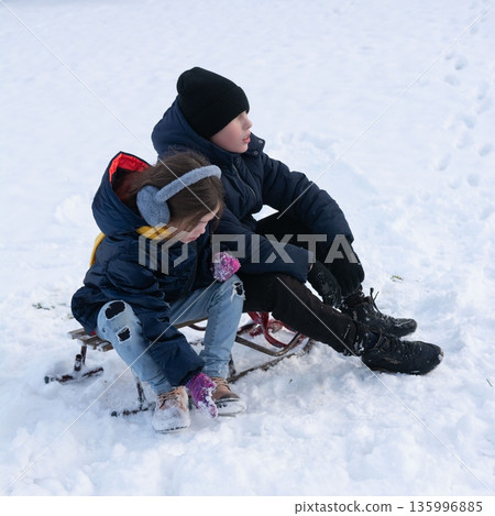 Siblings enjoy a snowy day sledding together, bundled in warm winter clothes. 135996885