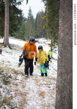 Winter adventure unfolds as an adult and child navigate snowy trails while carrying snowboards, ready for a playful day on the slopes in a scenic mountain landscape Winter adventure unfolds as an adult and child navigate snowy trails while carrying snowboards, ready for a playful day on the slopes in a scenic mountain landscape 135996942