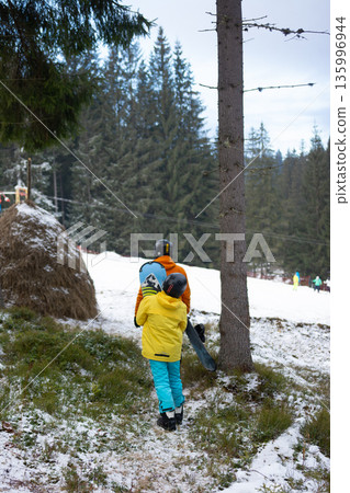 Excitement fills the air as a child and an adult prepare for a day of snowboarding in a beautiful winter landscape surrounded by towering trees Excitement fills the air as a child and an adult prepare for a day of snowboarding in a beautiful winter landscape surrounded by towering trees 135996944
