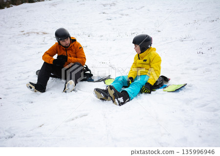 Enjoying a winter day on the snowy slopes, a father and son share laughter while sledding down hills in a picturesque snowy landscape Enjoying a winter day on the snowy slopes, a father and son share laughter while sledding down hills in a picturesque snowy landscape 135996946