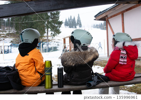 Friends admire the snowy slopes while wearing helmets, preparing for a thrilling day of skiing at a winter resort in the early morning 135996961