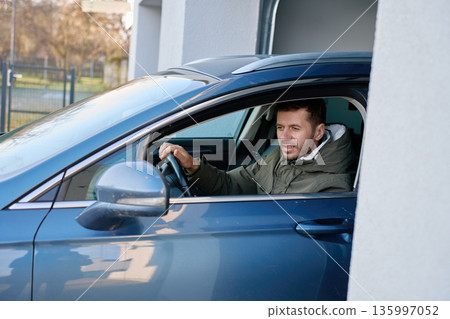 Man sitting in driver seat while driving car out of residential garage 135997052