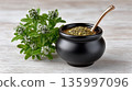 Mate tea sits in a black gourd next to fresh mint leaves on a wooden table 135997096