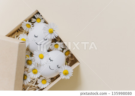 Cute Eggs with daisy flowers in a box on a yellow pastel background. Easter background. Cute Eggs with daisy flowers in a box on a yellow pastel background. Easter background. 135998080