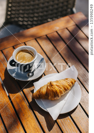 Cup of black coffee and a croissant on a table in a street cafe. Cup of black coffee and a croissant on a table in a street cafe. 135998249