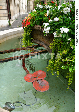 August 15, 2022: A street corner with a small fountain and flowers in the old town of Geneva, Switzerland August 15, 2022: A street corner with a small fountain and flowers in the old town of Geneva, Switzerland 135998300
