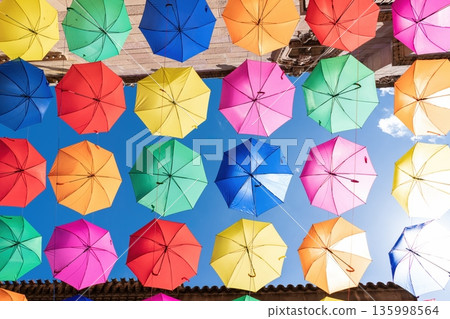Colorful umbrellas hanging overhead against blue sky 135998564