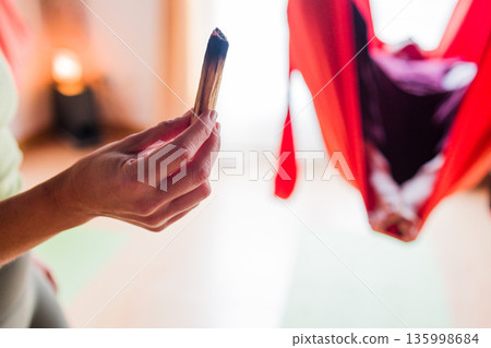Hand holding palo santo stick during aerial yoga Hand holding palo santo stick during aerial yoga 135998684