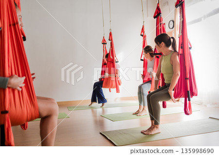 Multicultural women practicing aerial vinyasa yoga class 135998690