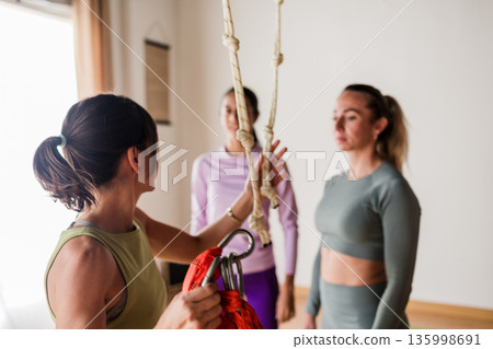 Instructor teaching aerial vinyasa yoga class with hammock 135998691