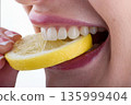 Close up of female teeth biting lemon slice showing ceramic veneers and natural dental care concept 135999404