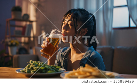 A Japanese woman enjoying a beer after a bath. Relaxing alone in the living room at home. 135999489