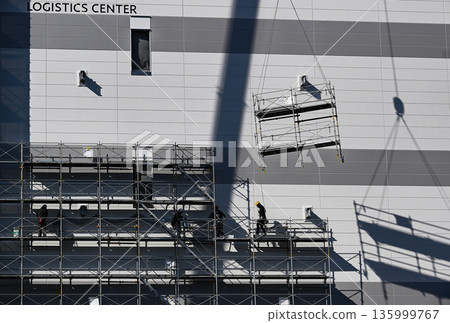Scaffolding removal work using a crane at a new logistics facility construction site Scaffolding removal work using a crane at a new logistics facility construction site 135999767