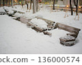 Snow-covered park bench and winter cityscape 136000574