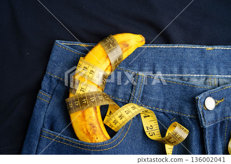 Banana with measuring tape on jean trousers, penis health. Banana with measuring tape on jean trousers, penis health. 136002041