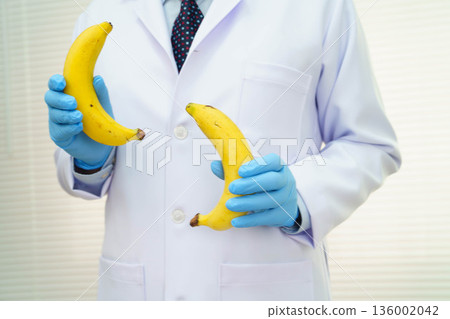 Male doctor stands holding a banana, penis health. Male doctor stands holding a banana, penis health. 136002042