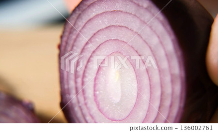 Slicing red onion with knife on board, showing detailed texture and rings. Fresh vegetable preparation concept  136002761