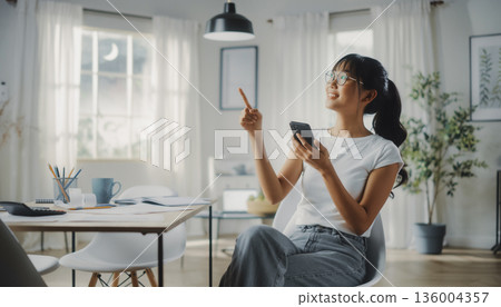 A smiling Japanese woman filing her tax return using her smartphone at home. Pointing pose and household management image 136004357