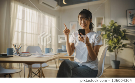 A smiling Japanese woman filing her tax return using her smartphone at home. Pointing pose and household management image 136004364