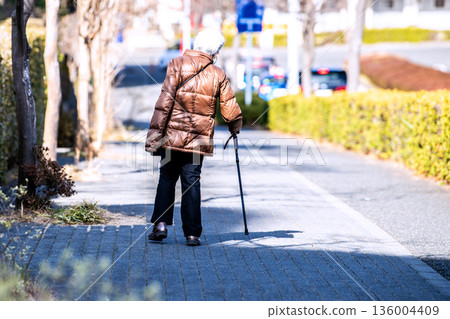 Yokohama cityscape in Japan: Light and shadow... Aging society: An elderly woman with a cane (wearing a mask). Her body leans to the right... Her left hand looks cold... 136004409