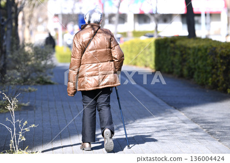 日本橫濱的城市景觀：光影交錯…老化社會：一位拄著拐杖的老婦人（戴著口罩）。她的身體向右傾斜……她的左手看起來冰冷…… 136004424